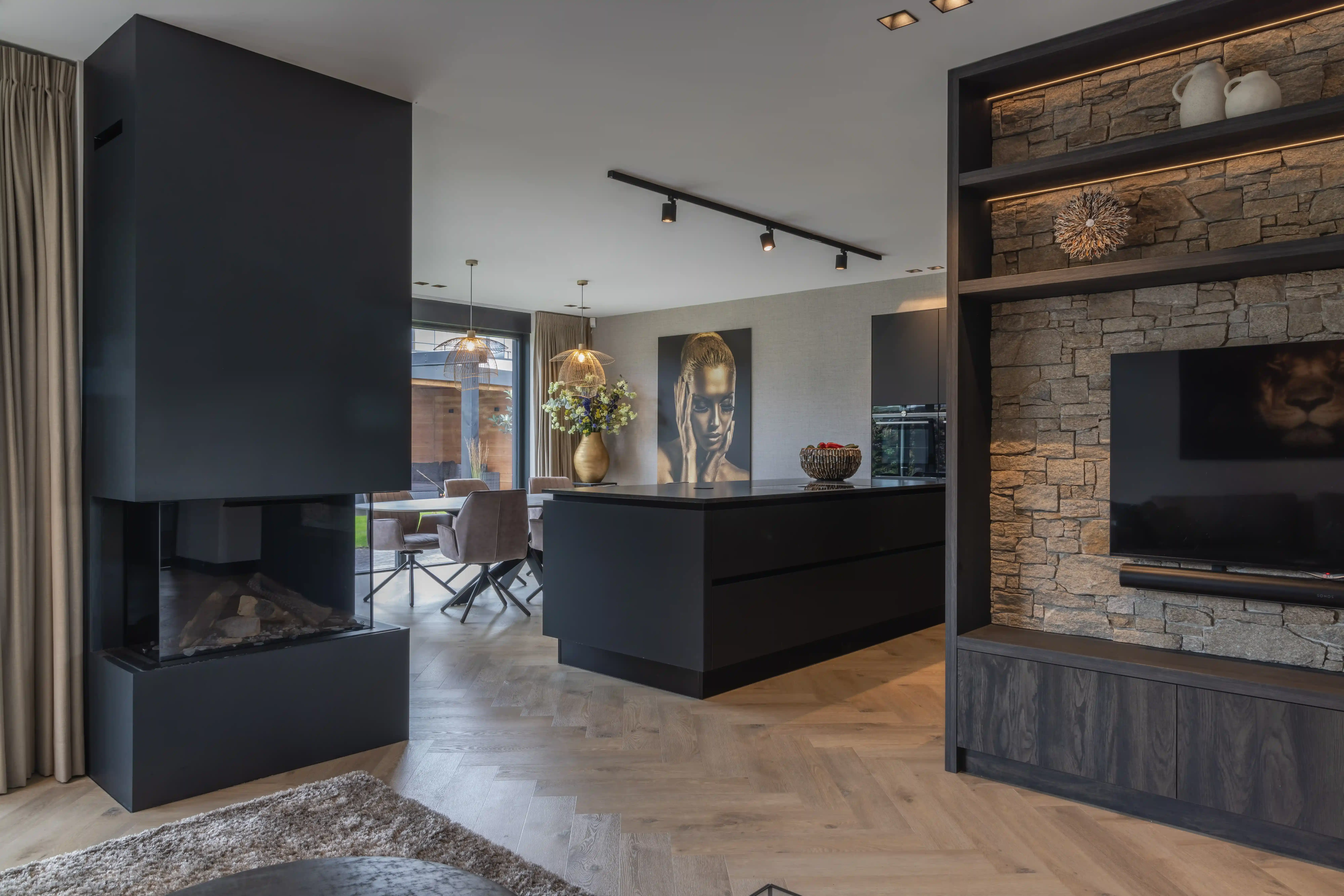 Villa Rotterdam - Open leefruimte met zwarte driezijdige haard, keukeneiland en stenen TV-wand